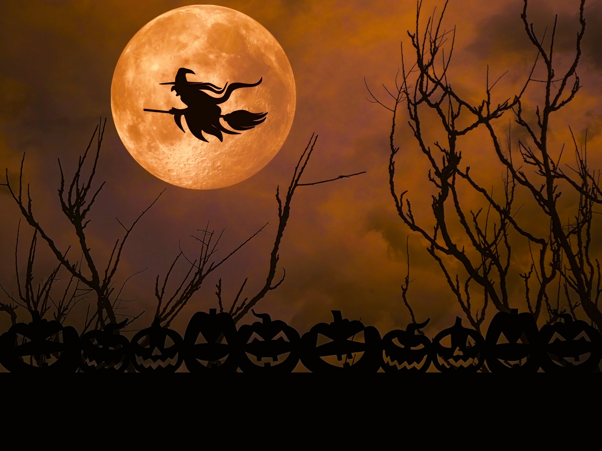 Halloween image of witch silhouetted flying in front of full moon with evil pumpkins at base